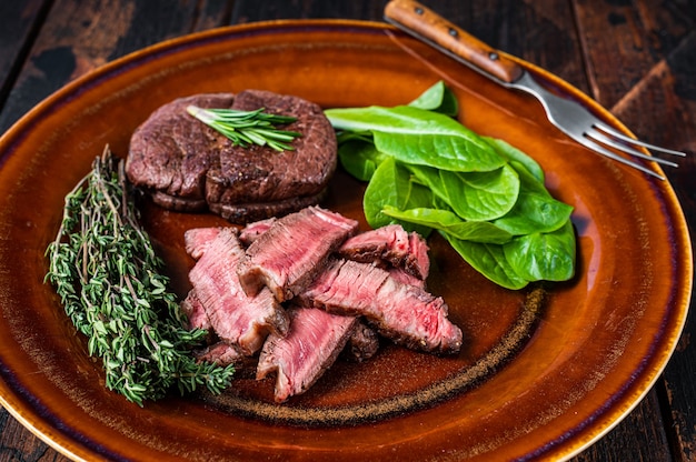 Filet Mignon Filet Braten und Fleisch Rindersteaks in einen Teller mit Salat schneiden. Dunkler hölzerner Hintergrund. Draufsicht.