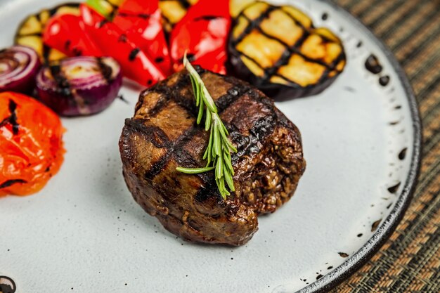 Filet mignon con verduras asadas y guarnición de romero en una placa blanca, close-up