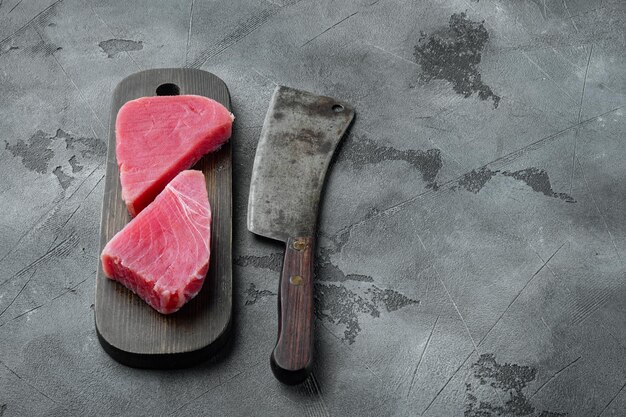 Filete de atún crudo ecológico. Conjunto de mariscos, sobre tabla de cortar de madera y viejo cuchillo de carnicero, sobre fondo de piedra gris, con copyspace y espacio para texto