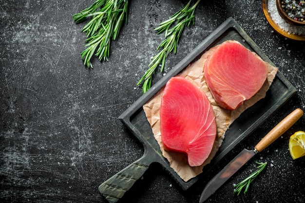 Filete de atún crudo en una tabla de cortar con especias y romero