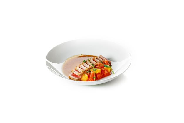Foto filete de atún jugoso cocido con verduras en una placa blanca sobre un fondo blanco.
