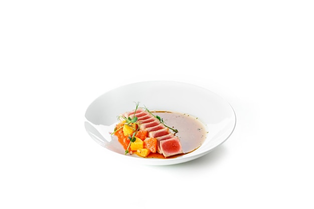 Filete de atún jugoso cocido con verduras sobre un fondo blanco.