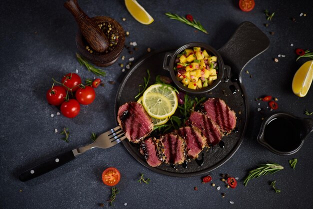 Filete de atún a la parrilla orgánico en rodajas cubierto con semillas de sésamo y salsa de mango en cerámica negra