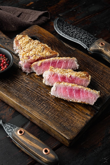 Filete de atún rojo raro a la parrilla con cebolletas y guisantes dulces, sobre tabla de servir de madera, sobre la vieja mesa de madera oscura.