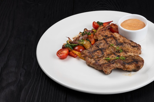 Filete de carne de cerdo a la parrilla en plato blanco sobre fondo de madera negra