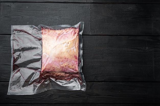 Filete de carne cruda de mármol cortado en envasado al vacío, sobre la mesa de madera negra, vista superior