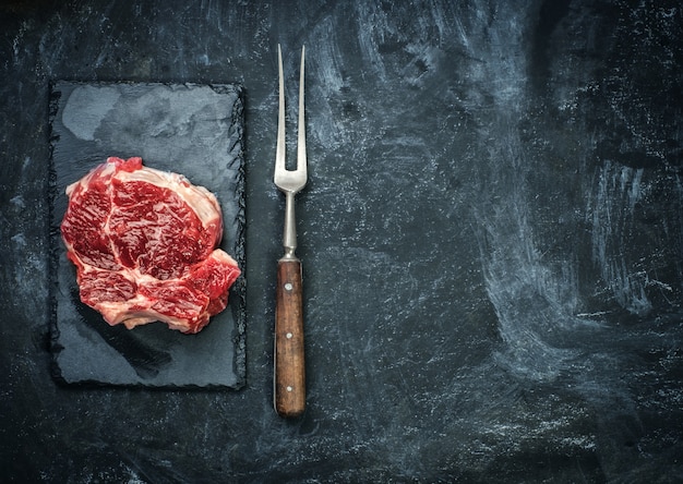 Filete de carne cruda en la placa de piedra sobre la mesa negra.