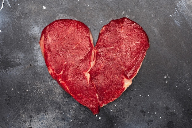 Filete de carne fresca cruda en forma de corazón sobre una superficie oscura, vista superior.