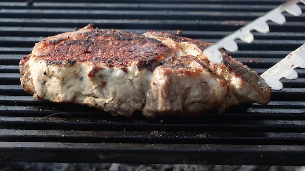 Un filete de carne frito en una rejilla con humo y fuego.