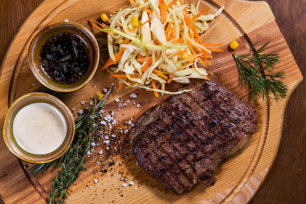 Filete de carne grande con verduras, vegetación y salsas en una mesa de madera en un restaurante de lujo