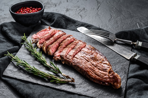 Filete de carne de res asada en una tabla de piedra negra. Fondo negro. Vista superior