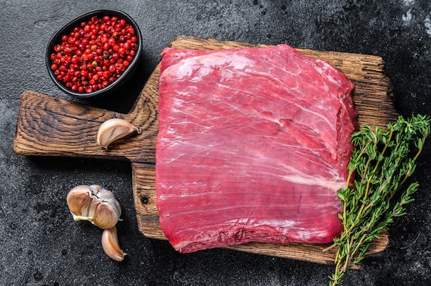 Filete de carne de res cruda flanco o solapa sobre una tabla de cortar de madera. Fondo negro. Vista superior.