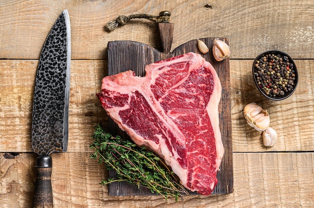 Filete de carne de res cruda Porterhouse o T-bone con hierbas sobre una tabla de cortar de madera. fondo de madera. Vista superior.