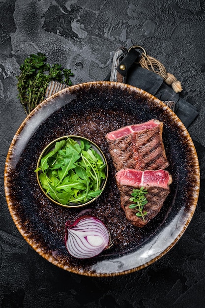 Filete de carne de res de ostra a la parrilla en un plato con ensalada Fondo negro Vista superior