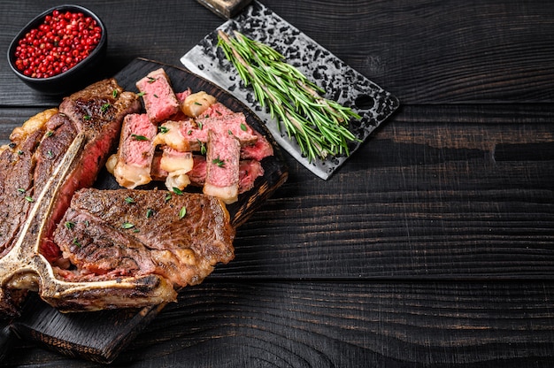 Filete de carne de res en rodajas y asado T-bone o porterhouse para el menú del asador. Fondo de madera negra. Vista superior. Copie el espacio.