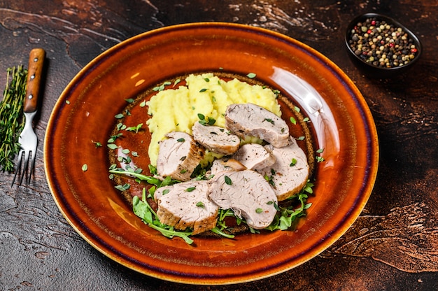 Filete de carne de solomillo de cerdo asado en un plato con puré de patatas. Fondo oscuro.