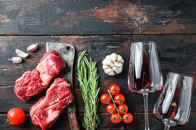 Filete de carne de vacuno crudo orgánico tirado sobre viejo cuchillo de carnicero cerca de copas de vino tinto con hierbas y condimentos en la vieja mesa de madera oscura. Vista superior, con espacio para texto.