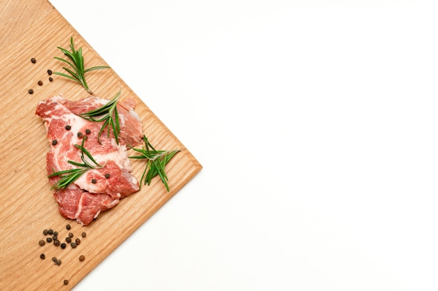 Filete de carne de vacuno fresca cruda con romero y pimienta en la tabla de cortar aislada sobre fondo blanco, espacio de copia, cocinando alimentos en casa.