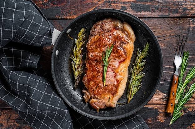 Filete de carne de vacuno a la parrilla en una sartén con hierbas. Fondo de madera oscura. Vista superior.