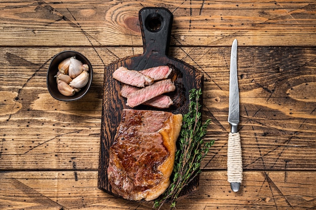 Filete de carne de vacuno en tiras de Nueva York a la parrilla en rodajas o lomo en una tabla de madera. fondo de madera. Vista superior.