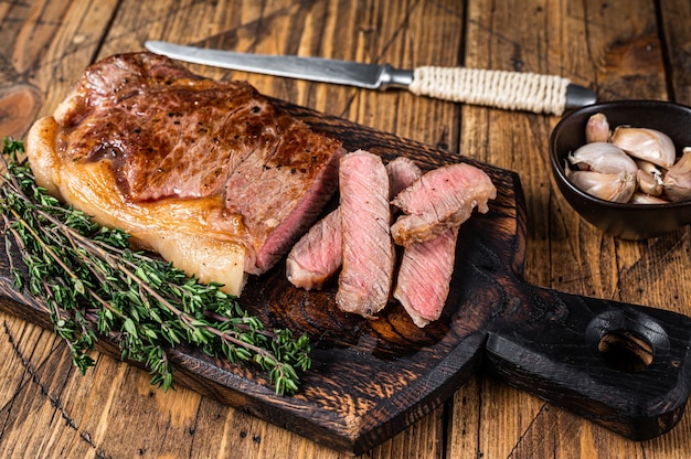 Filete de carne de vacuno en tiras de Nueva York a la parrilla en rodajas o lomo en una tabla de madera