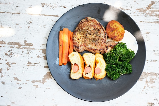 Filete de carne con verduras asadas y especias colocadas en un plato sobre una mesa de madera