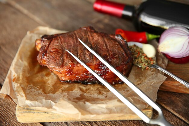 Filete de cerdo asado con botella de vino tinto y tenedor de carne sobre fondo de madera