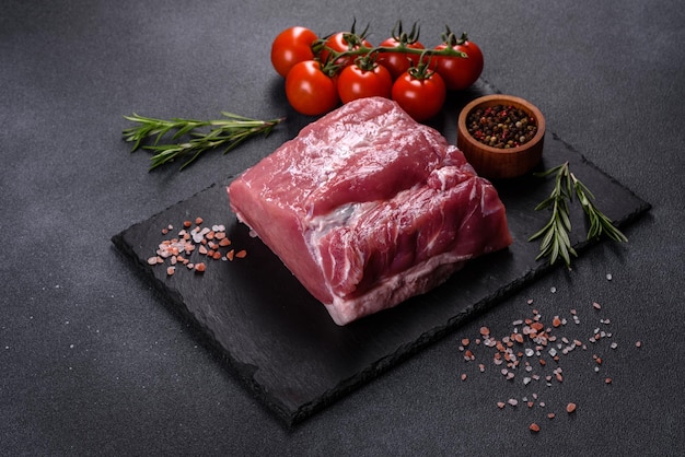 Filete de cerdo crudo sobre una tabla de cortar con hierbas y especias en la mesa de piedra oscura