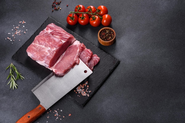 Filete de cerdo crudo sobre una tabla de cortar con hierbas y especias en la mesa de piedra oscura