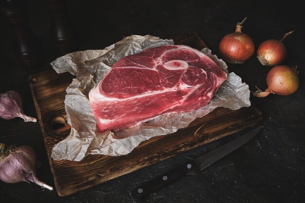 Filete de cerdo crudo sobre una vieja tabla de cortar, cuchillo, especias e ingredientes se colocan uno al lado del otro.