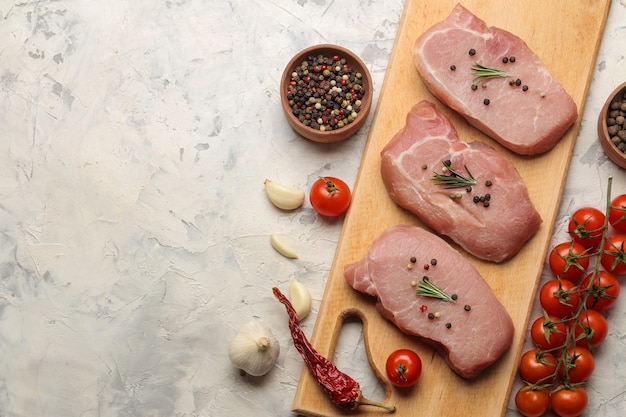 Filete de cerdo crudo en el tablero, carne e ingredientes para cocinar, especias, hierbas y verduras sobre un fondo claro. vista superior. espacio para texto