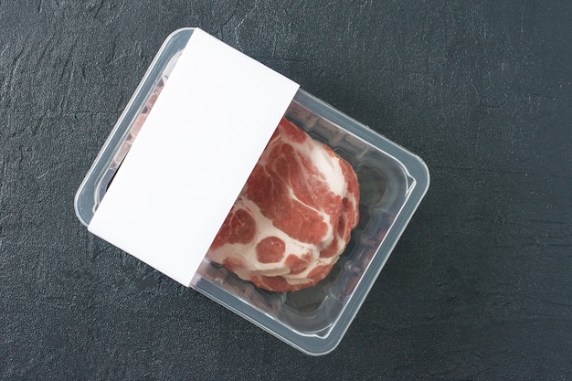 Filete de cerdo crudo veteado en envasado al vacío sobre fondo negro, vista superior, maqueta de logotipo para el diseño