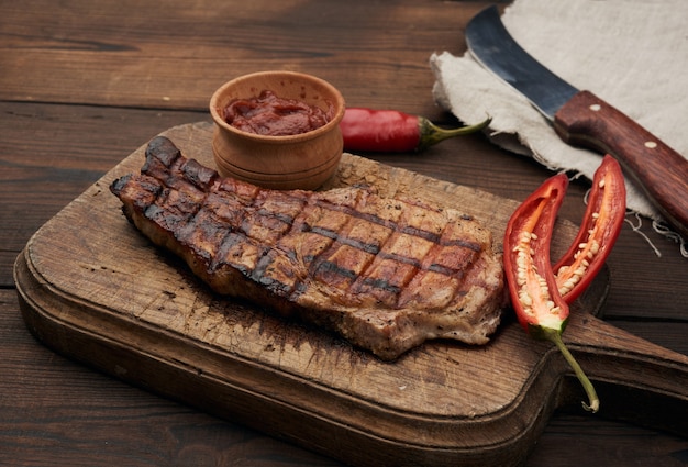 El filete de cerdo frito en la costilla se encuentra en una tabla de madera marrón vintage, junto a los chiles rojos frescos