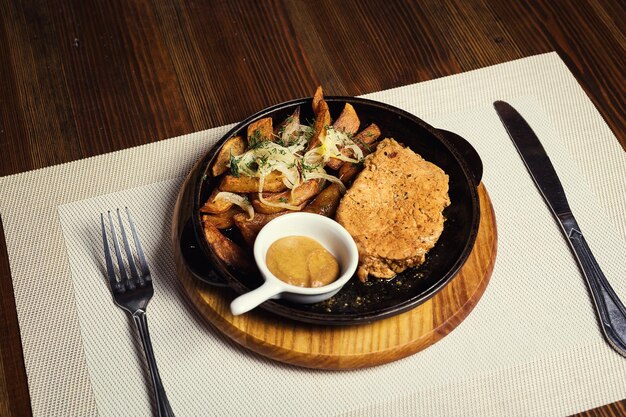 Filete de cerdo con patatas fritas en una sartén servido con salsa de mostaza en un restaurante