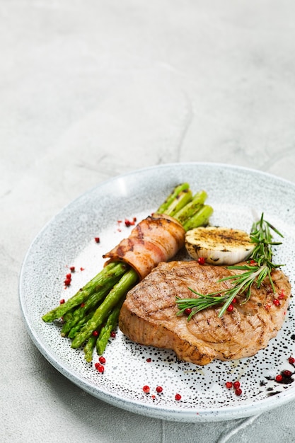 Filete de cerdo a la plancha con espárragos y hojas de romero en la mesa de hormigón de cerca.