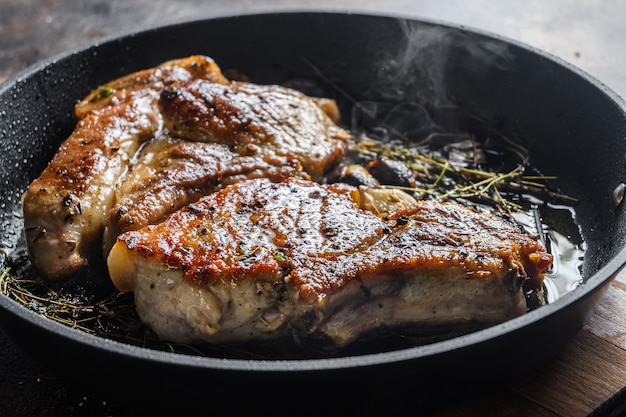 Filete de cerdo a la plancha con hueso con condimentos en sartén caliente con humo