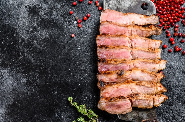 Filete de cerdo en rodajas a la parrilla en una cuchilla de carne. Carne orgánica Fondo negro.