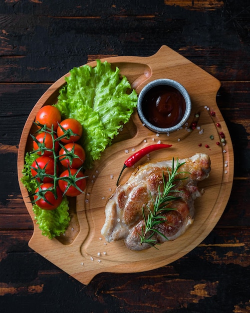 Filete de cerdo en una tabla de madera con tomates cherry y ensalada de comida rústica