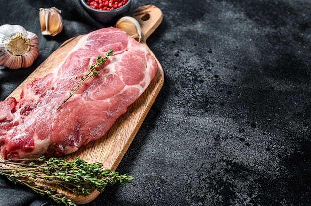 Filete de chuleta de cerdo cruda. Pedazo de carne cruda lista para preparar con verduras y especias. Fondo negro.