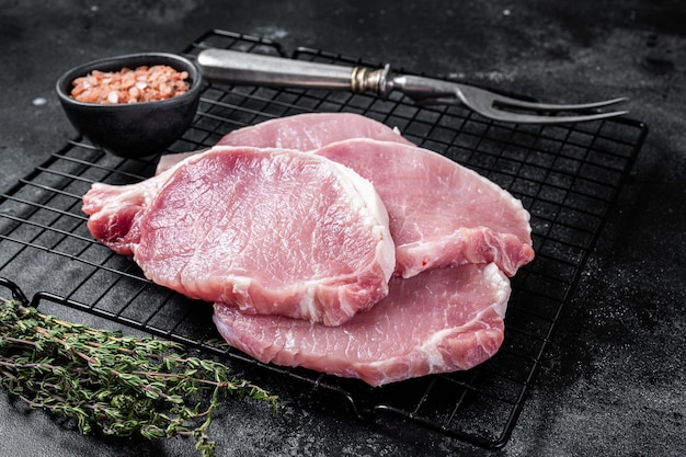 Filete de chuleta de cerdo crudo para freír en una sartén con hierbas Fondo negro Vista superior