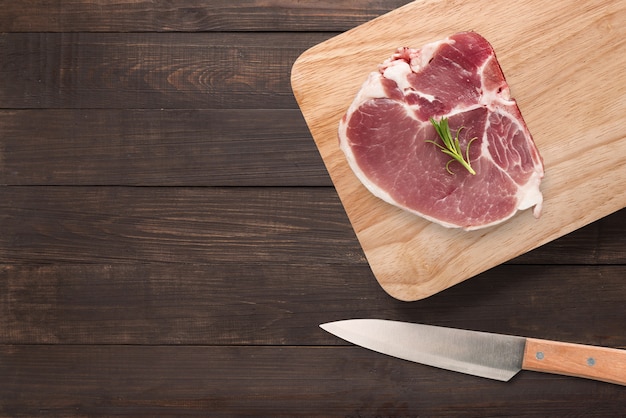 Filete de chuleta de cerdo crudo vista superior en tabla de cortar y cuchillo sobre fondo de madera. Copyspace para tu texto