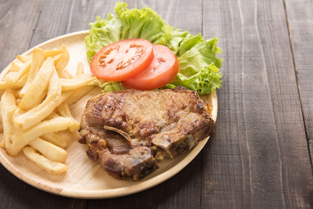 Filete de chuleta de cerdo a la parrilla y verduras con papas fritas en la mesa de madera.