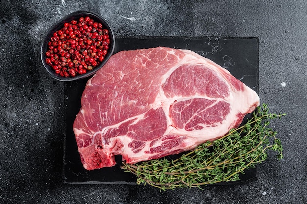 Filete de cuello de cerdo de carne cruda en tablero de mármol con hierbas Fondo negro Vista superior