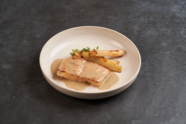 Filete de esturión al horno con espinacas en un plato blanco sobre mesa gris