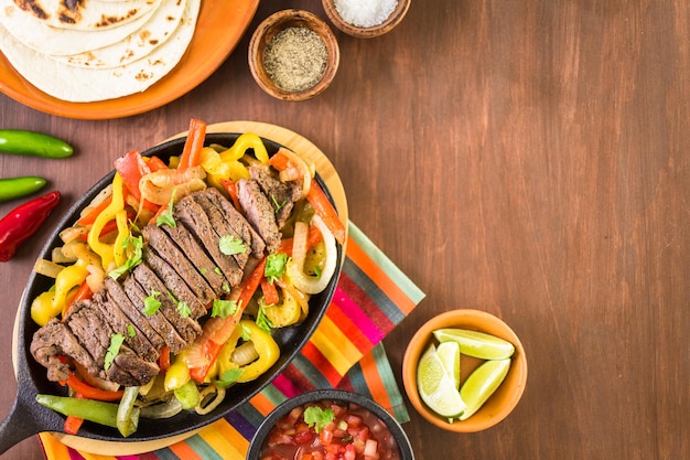 Foto filete de fajitas con pimientos morrones y cebolla amarilla en una sartén de hierro fundido para fajitas.