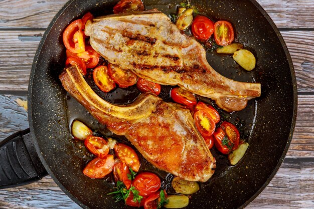 Filete frito con tomate y ajo en sartén sobre madera.