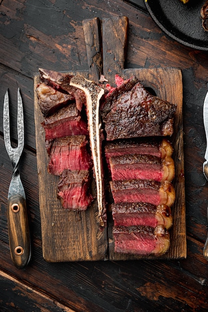 Filete de hueso t en rodajas a la parrilla, sobre tabla de servir de madera, sobre la vieja mesa de madera oscura.