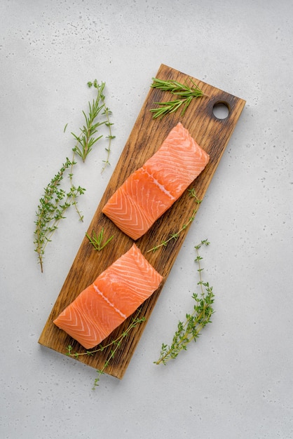 Filete jorobado de salmón crudo fresco sobre placa de madera tomillo romero sal pimienta encima