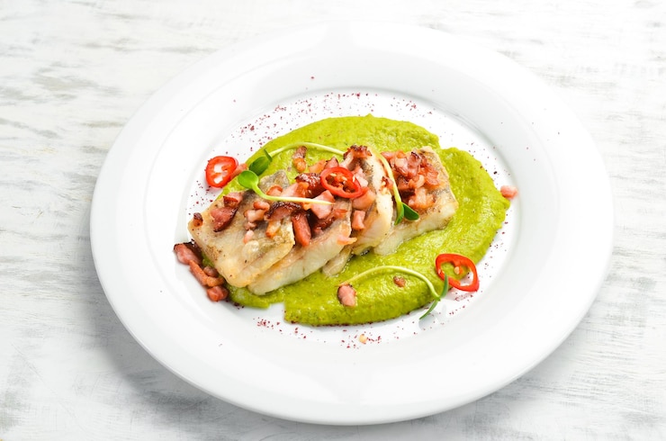 Foto filete de merluza al horno y tocino con guarnición de espinacas en un plato blanco vista superior