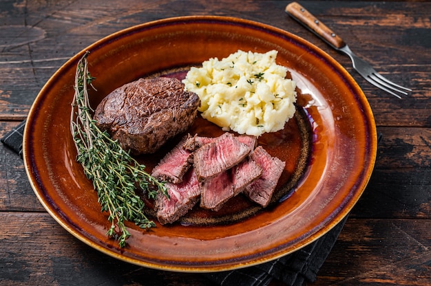 Filete mignon en rodajas o solomillo de ternera en un plato rústico con puré de patatas. Fondo de madera oscura. Vista superior.